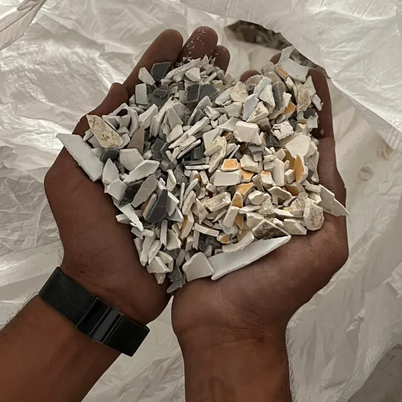 Hands holding grey and white PVC pipe regrind over a bulk bag