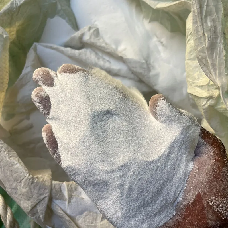 Hand holding white LG off-grade PVC resin powder over an open bag