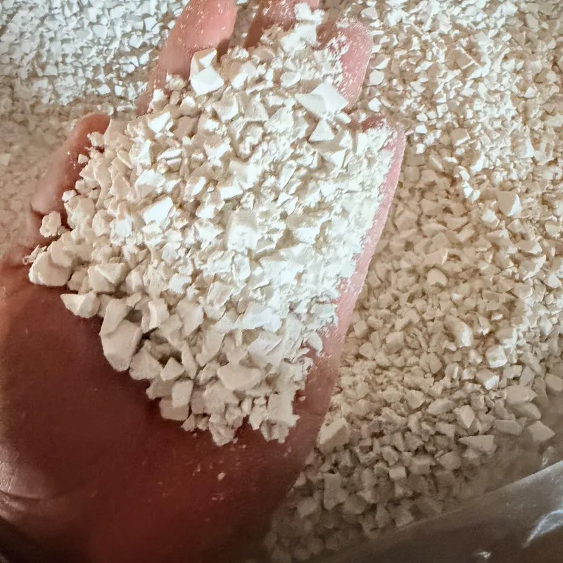 Hand holding white PVC pipe regrind over a bulk bag