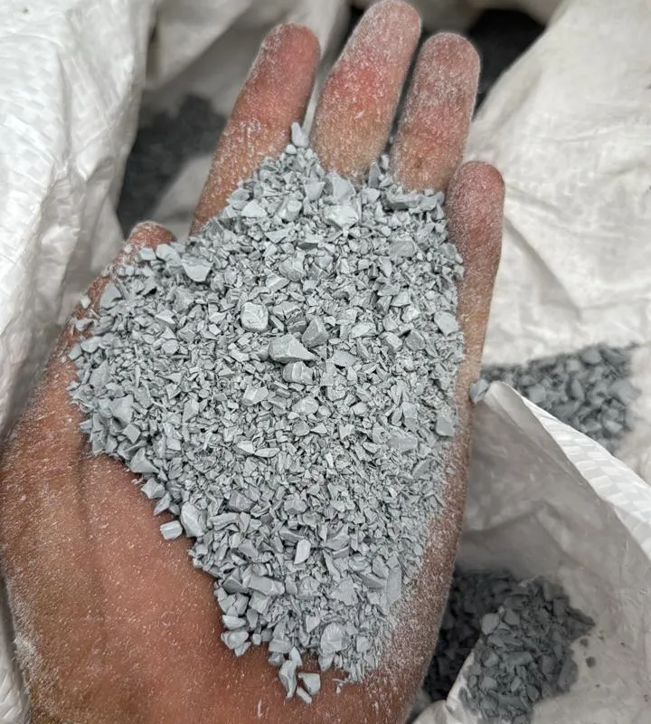 Hand holding light grey PVC moulding regrind over a bulk bag
