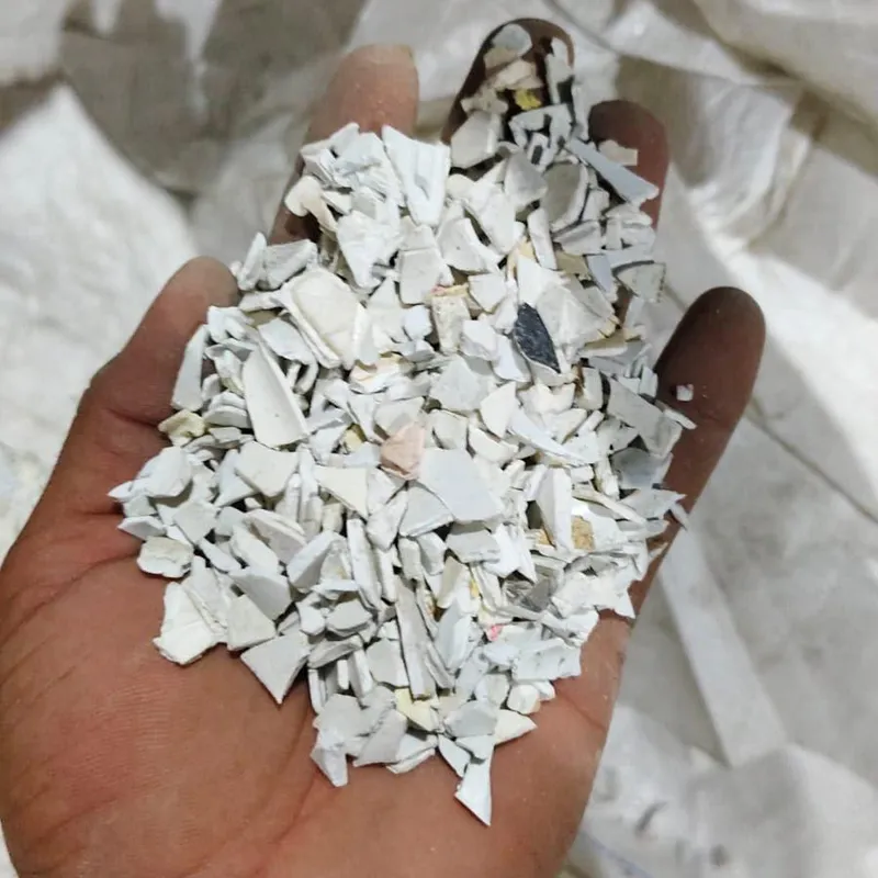 Hand holding white PVC pipe regrind over a bulk bag