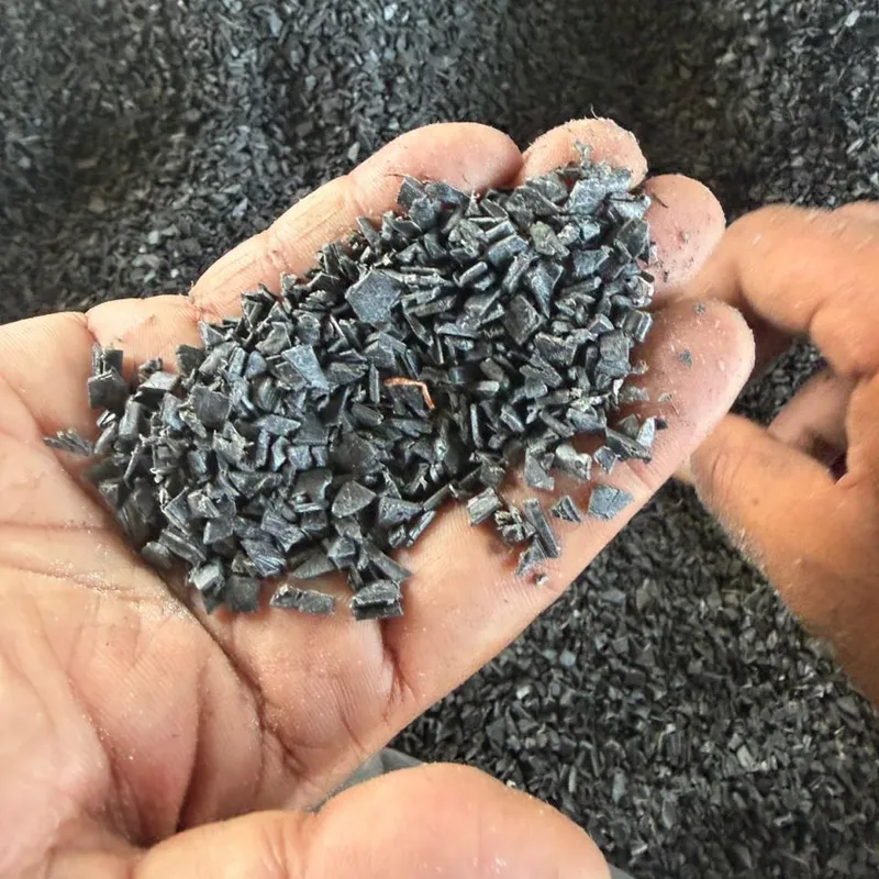 Hands holding black PVC window profile regrind over a bulk bag